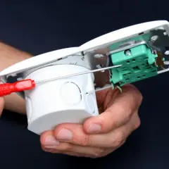 Ręce montują puszkę instalacyjną, podłączając zasilanie z włącznika światła.