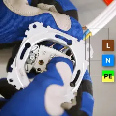 Ręce w rękawicach montują mechanizm, pokazując schemat wyłącznika schodowego potrójnego z oznaczeniami przewodów L, N, PE.