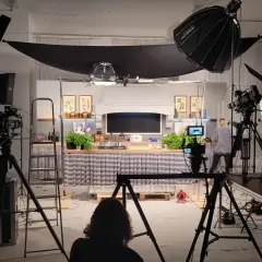 Studio filmowe z kuchnią, kamerami i lampami. Widać tu moc światła, które tworzy atmosferę do nagrania.