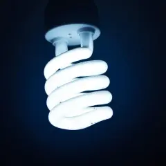 Świeci żarówka energooszczędna, jej spiralne ramiona emanują chłodnym, niebieskawym światłem.
