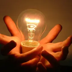 Dwie dłonie trzymają świecącą żarówkę. Czy 2000 lumenów to dużo? To jasne jak słońce!