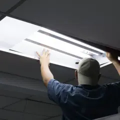 Pracownik w czapce wymienia świetlówki na led w suficie podwieszanym.