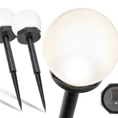Dwie białe lampy solarne w kształcie kuli z czarnymi tyczkami. Na dole jednej z lamp widać panel solarny, który ładuje się od słońca, a nie od żarówki.