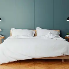 Elegancka sypialnia z białym pościelonym łóżkiem. Po obu stronach łóżka, na odpowiedniej wysokości, zamontowano czarne kinkiety, tworząc przytulną atmosferę.