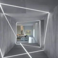 Nowoczesny korytarz z betonowymi ścianami i geometrycznym podświetleniem ściany od dołu. W tle salon z kominkiem i widokiem na zieleń.