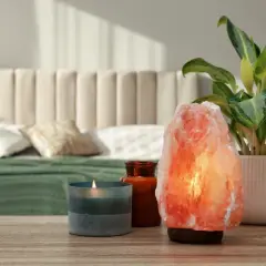 Różowa lampa solna właściwości relaksacyjne, obok świeca i roślina. Sypialnia w tle.
