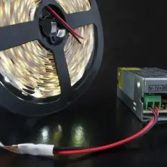 Zasilacz do taśmy LED 12V GU10 i zwinięta taśma LED na czarnym tle.
