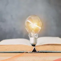 Żarówka rozświetla otwartą księgę, symbolizując idealne światło do czytania i narodziny pomysłów.