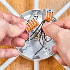 Ręce łączą przewody w puszce sufitowej, pokazując jak podłączyć halogeny w suficie schemat.