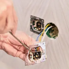 Ręce majsterkowicza przykręcają mechanizm gniazdka, pokazując, jak przerobić włącznik pojedynczy na podwójny.