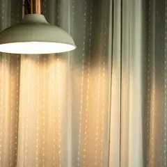Jasna lampa wisząca rzuca ciepłe światło na zasłony. Czy 3000 lumenów to dużo? To zależy od pomieszczenia, ale ta lampa z pewnością rozjaśnia przestrzeń.
