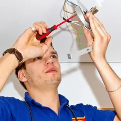 Mężczyzna z wkrętakiem przy suficie, podłączający przewody. Instrukcja jak wymienić żyrandol krok po kroku.