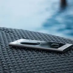Smartfon z kroplami wody na ekranie, leżący na plecionej powierzchni. To dowód, że ip68 co to znaczy: ochrona przed wodą i pyłem.
