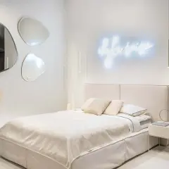 Nowoczesne oświetlenie sypialni inspiracje: neonowy napis, wiszące lampy i lustra o organicznych kształtach tworzą przytulną atmosferę.