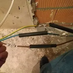 Ręczne skręcanie kabli elektrycznych, przygotowanie do izolacji. Widać połączenia przewodów w trakcie pracy.