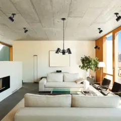 Nowoczesny salon z betonowym sufitem, gdzie oświetlenie ogólne tworzą reflektory. Widok na góry.