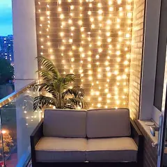 Ciepłe światła tworzą przytulny pomysł na oświetlenie balkonu. Sofa i palma dodają uroku.