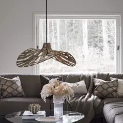Pleciona lampa wisząca tworzy przytulne oświetlenie nad stołem w salonie, gdzie króluje szara sofa z poduszkami i pledem.