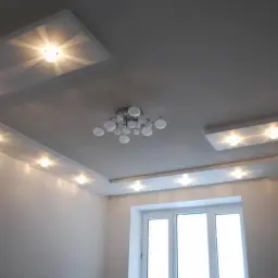 Nowoczesny sufit podwieszany z oświetleniem punktowym rozmieszczonym w równych odstępach, tworzącym subtelne światło. Centralnie wisi designerska lampa.