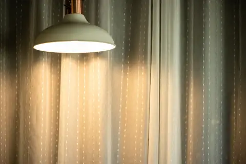 Jasna lampa wisząca rzuca ciepłe światło na zasłony. Czy 3000 lumenów to dużo? To zależy od pomieszczenia, ale ta lampa z pewnością rozjaśnia przestrzeń.