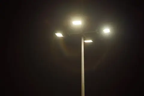 Słup oświetleniowy z czterema lampami LED, które rozświetlają noc. Widać tęczowe refleksy, jakby porównanie lampa sodowa vs led.