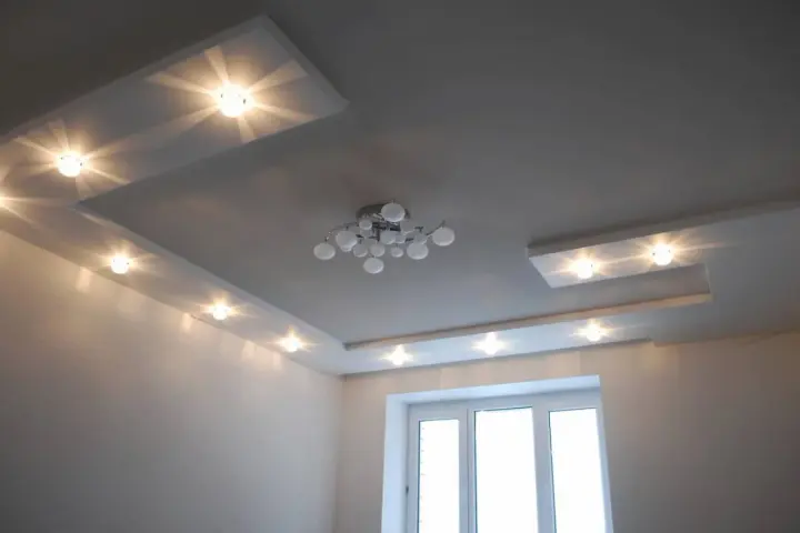 Nowoczesny sufit podwieszany z oświetleniem punktowym rozmieszczonym w równych odstępach, tworzącym subtelne światło. Centralnie wisi designerska lampa.