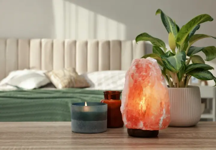 Różowa lampa solna właściwości relaksacyjne, obok świeca i roślina. Sypialnia w tle.