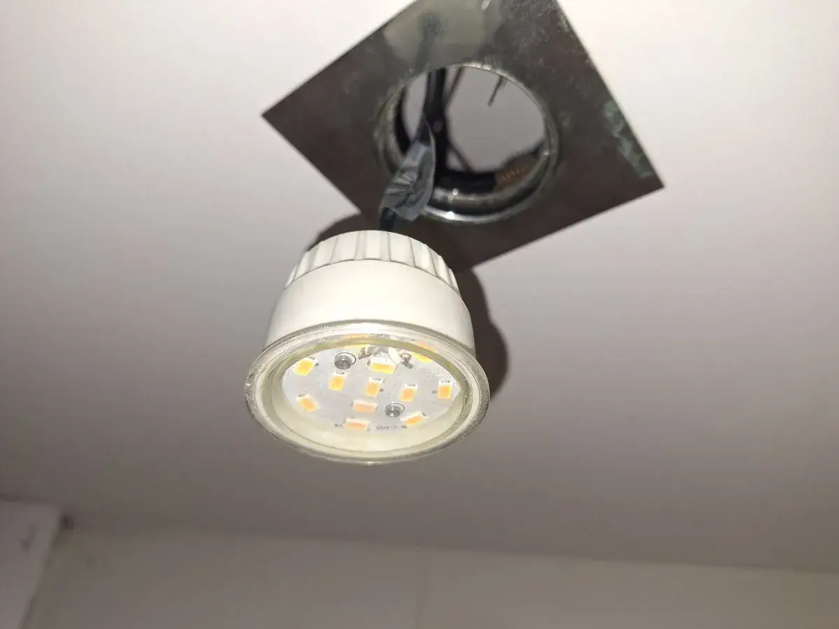 Wymiana żarówki LED GU10: widoczna jest nowa żarówka LED GU10 wisząca obok oprawy sufitowej, gotowa do montażu.