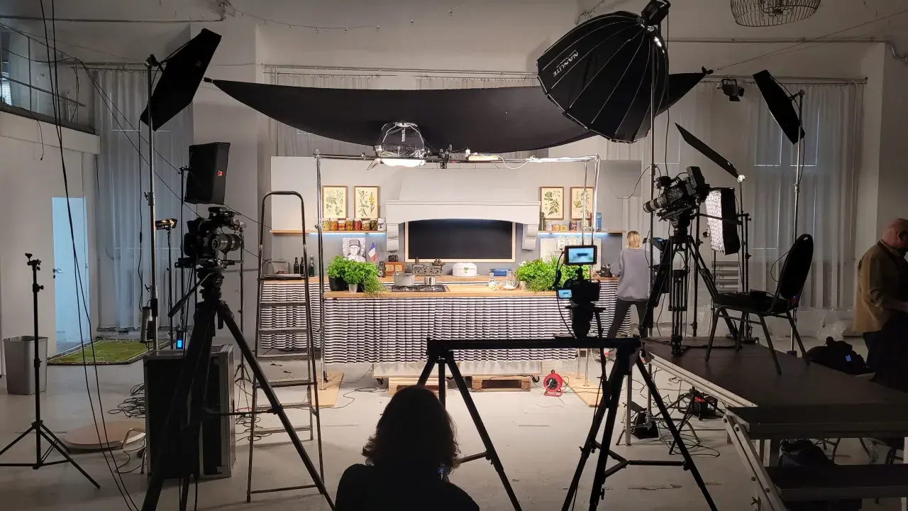 Studio filmowe z kuchnią, kamerami i lampami. Widać tu moc światła, które tworzy atmosferę do nagrania.