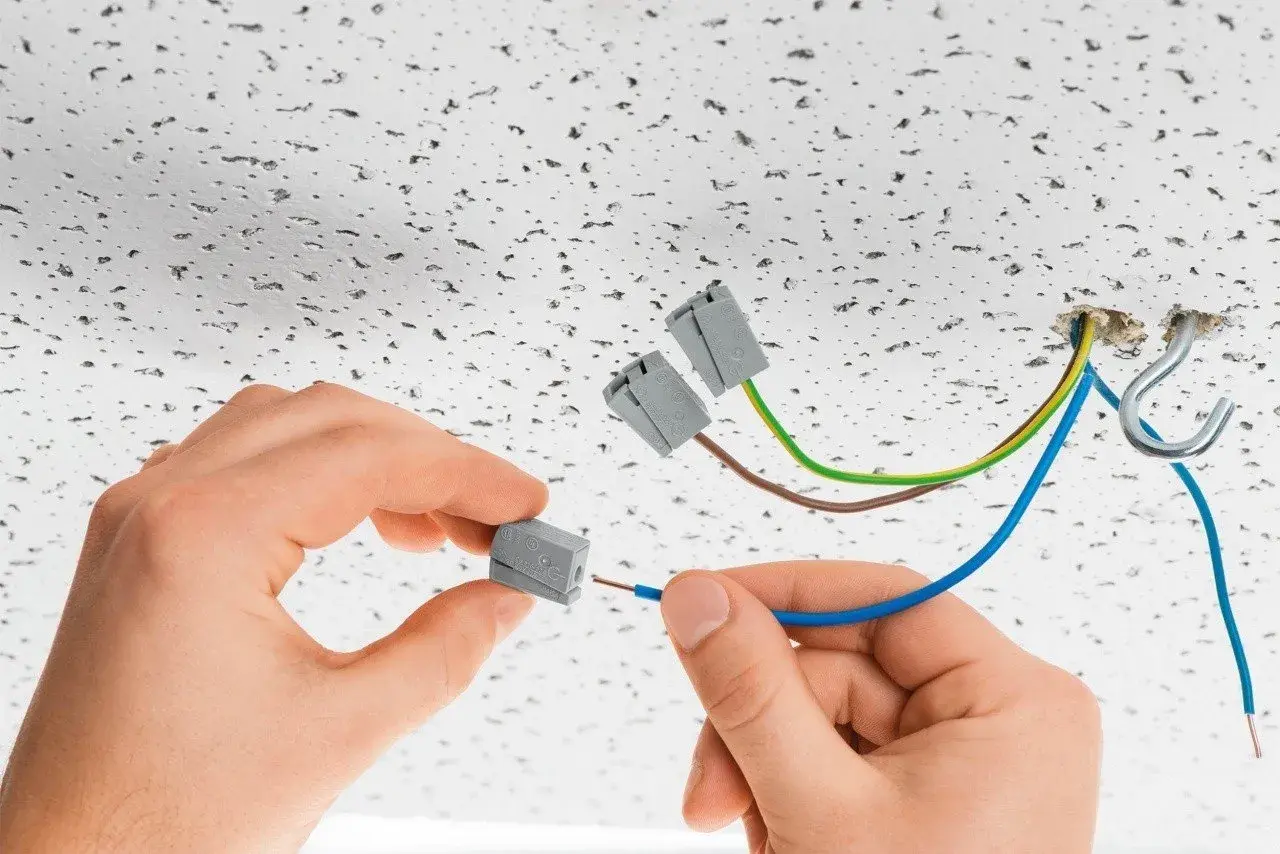 Ręce montują przewody do złączek elektrycznych. To szybkie i bezpieczne rozwiązanie, czy to wago czy kostka, ułatwia instalację.