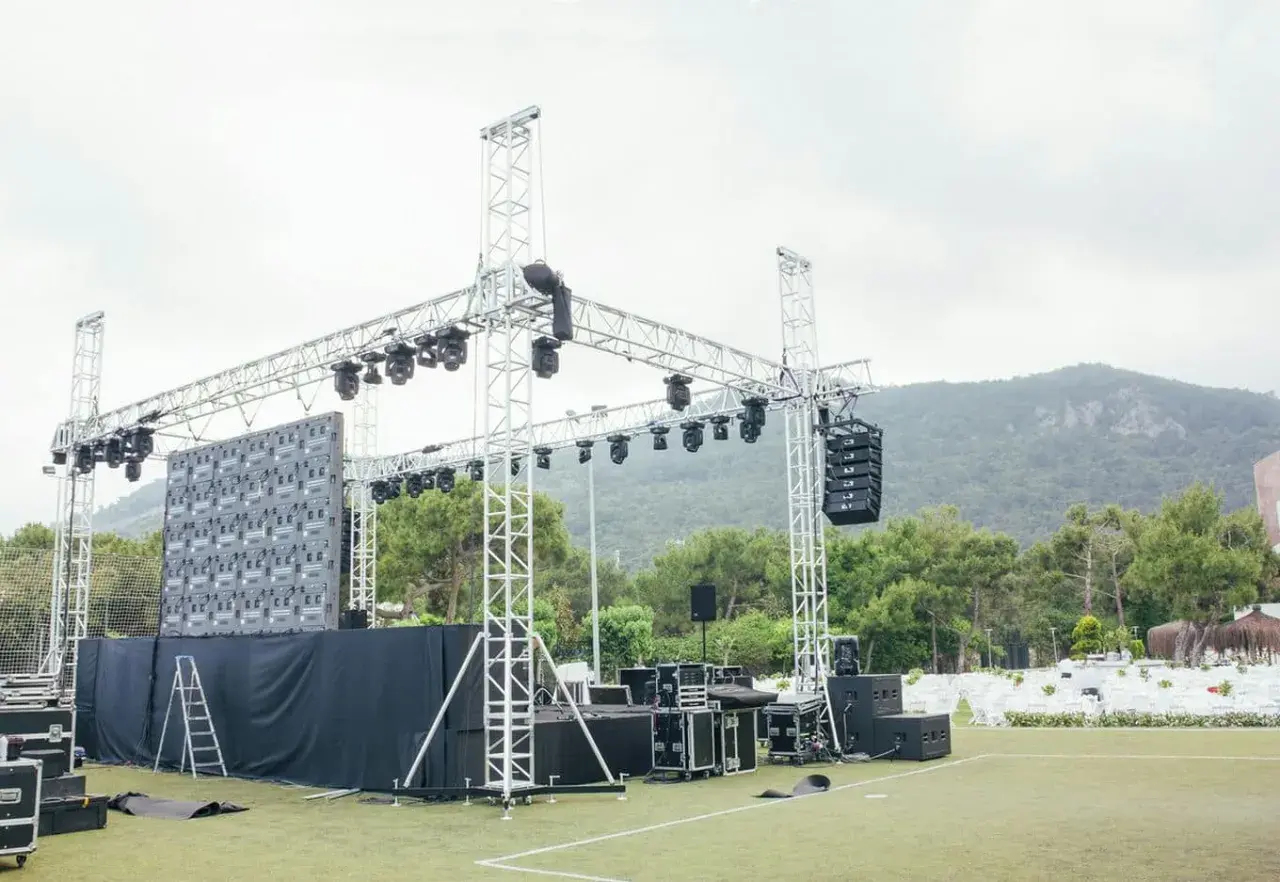 Scena z ekranem LED i różnymi rodzajami oświetlenia scenicznego, głośnikami i konstrukcjami aluminiowymi, gotowa na wydarzenie.