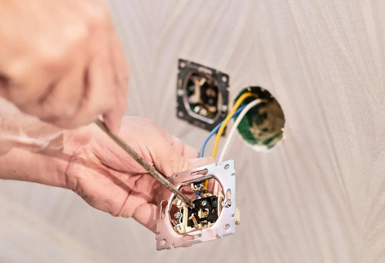 Ręce majsterkowicza przykręcają mechanizm gniazdka, pokazując, jak przerobić włącznik pojedynczy na podwójny.