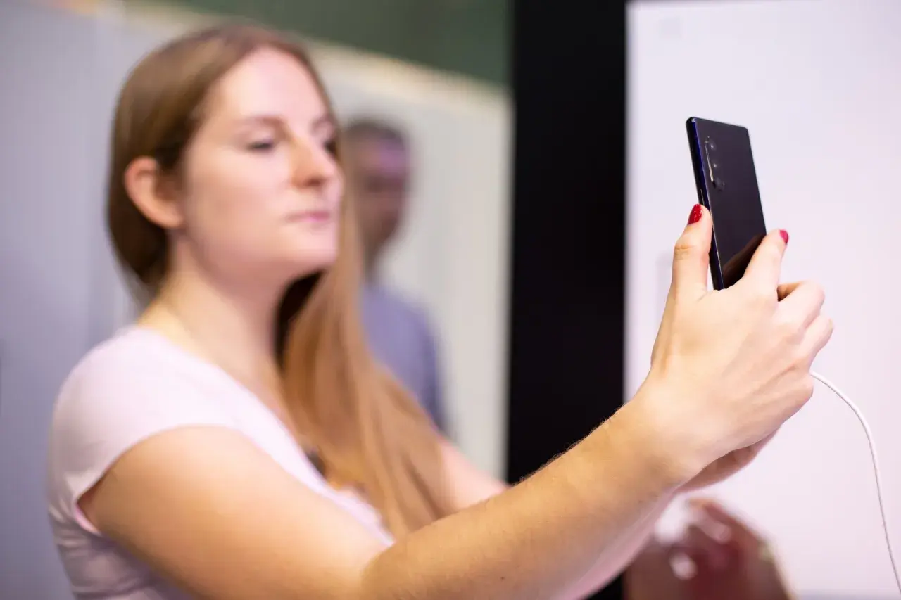 Kobieta z długimi blond włosami trzyma smartfon, na którym widać **aplikację Tuya po polsku**.