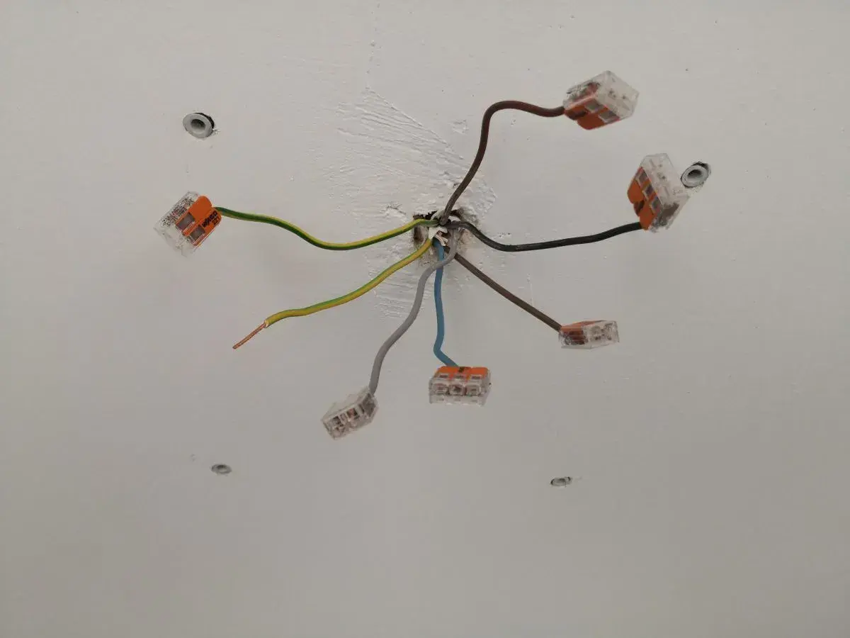 Sufit z instalacją elektryczną. Widać kilka przewodów, w tym jeden brązowy, połączonych złączkami.