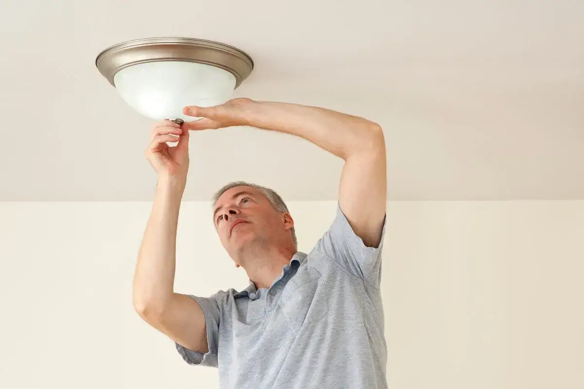 Mężczyzna wymienia żarówkę w tubie lampy sufitowej.