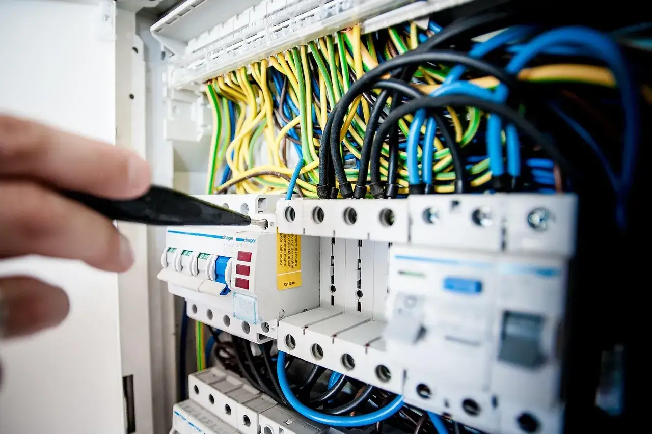Ręka z narzędziem przyłącza przewody do kostki do kabli w rozdzielnicy elektrycznej.