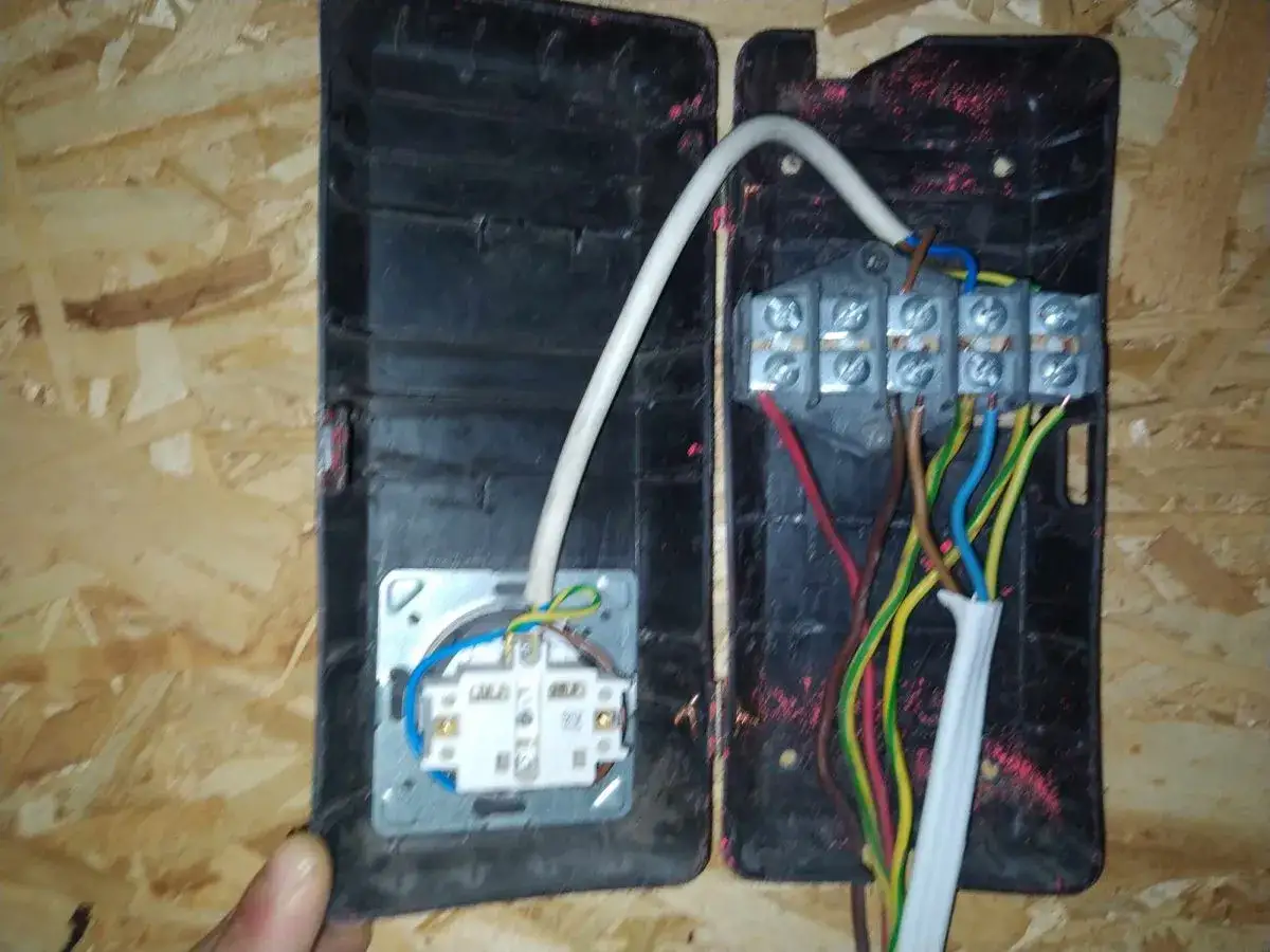 Widok na otwartą puszkę elektryczną z widocznymi, kolorowymi przewodami. Stare kolory kabli elektrycznych, takie jak brązowy, niebieski, zielono-żółty i czerwony, łączą się w zaciskach.