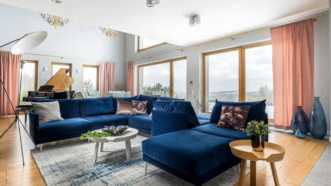 Elegancki salon z granatową kanapą i fortepianem. Nad narożnikiem zamontowano stylowe oświetlenie, które dodaje wnętrzu blasku.