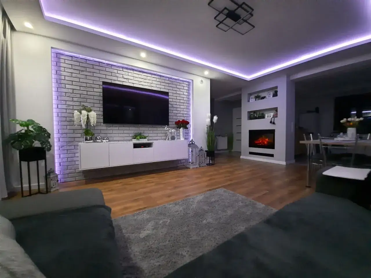 Nowoczesne oświetlenie ściany z telewizorem w salonie, podkreślające ceglaną fakturę i tworzące nastrojową atmosferę.