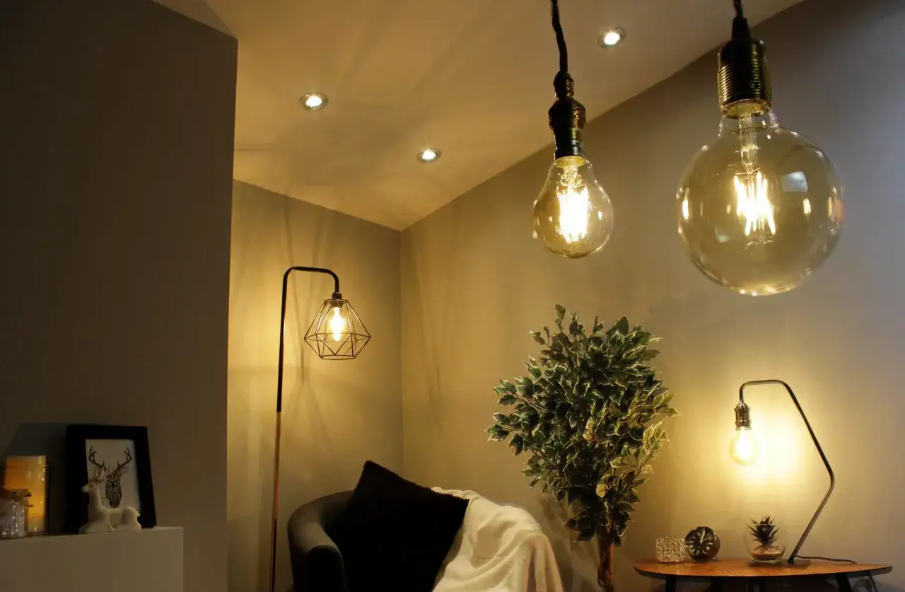 Dwie wiszące żarówki z widocznym żarnikiem, lampa podłogowa i stołowa tworzą przytulną atmosferę.
