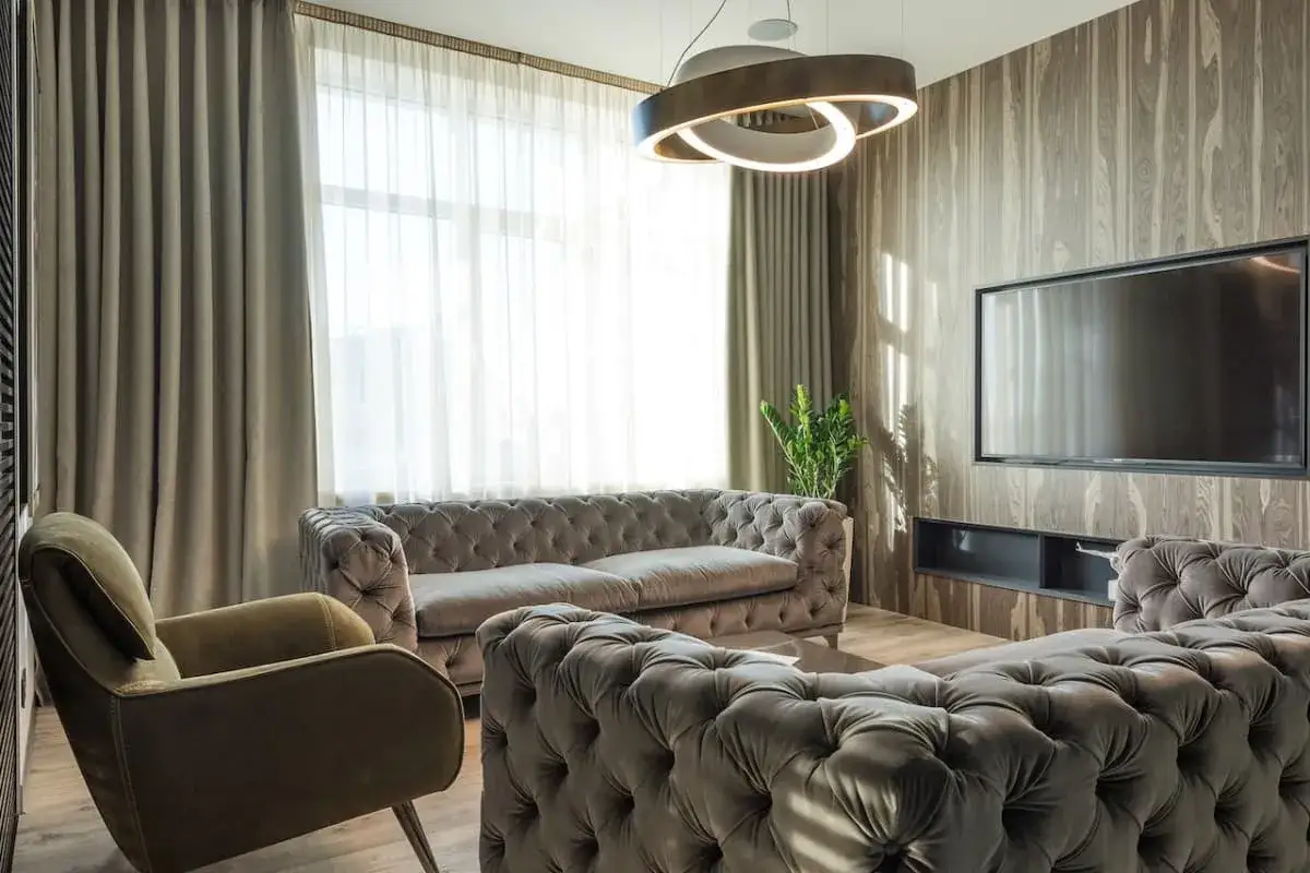 Nowoczesny salon z szarymi sofami i fotelem. Nad nimi wisi designerski żyrandol, idealny jako inspiracja, jaki żyrandol do salonu wybrać.