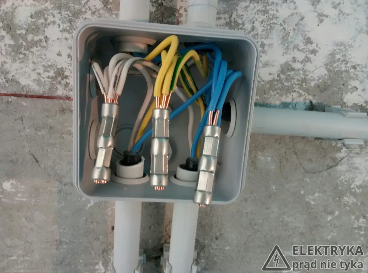 Instrukcja jak zmostkować kable: połączenie przewodów w puszce elektrycznej, widoczne miedziane końcówki i izolacje.